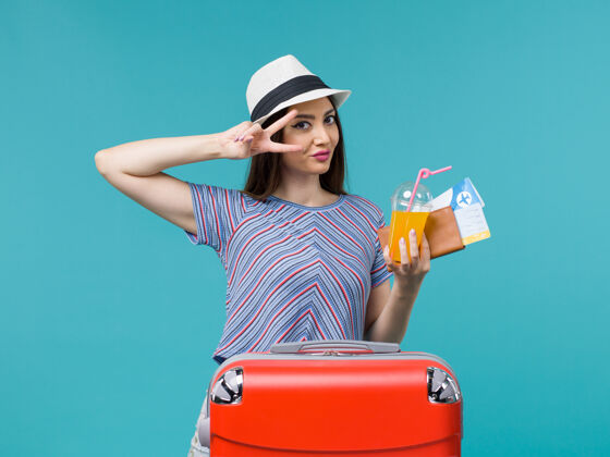 包前视图：度假中的女人拿着她的红色袋子 拿着蓝色背景的机票和果汁 旅行 度假 女人旅行旅行微笑女