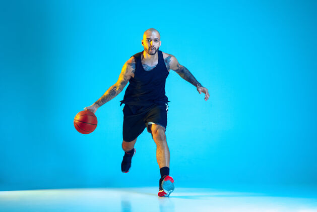 游戏年轻的篮球队员穿着运动服训练 在行动中练习 在霓虹灯下隔离在蓝色的墙上篮球活跃运动装