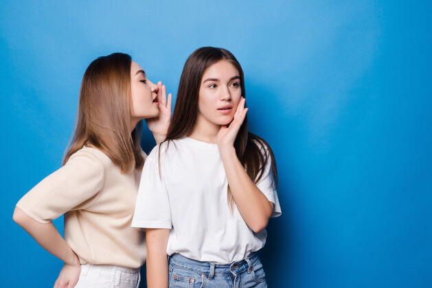 女性年轻的女人对她的伴侣低声说坏消息隔离在蓝色的墙上说话黑发年轻