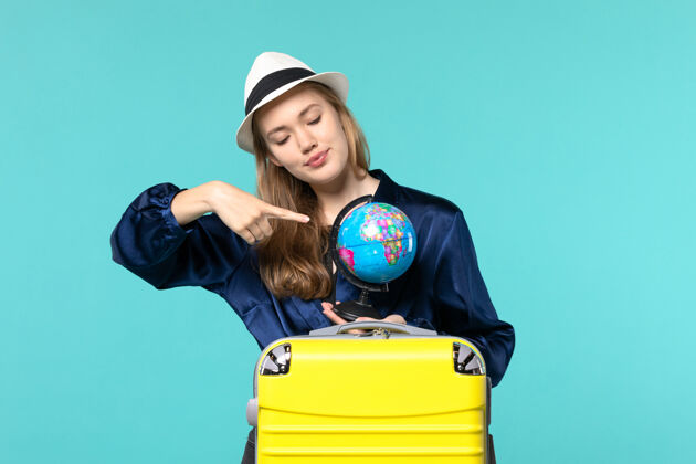 手持正面图年轻女子手持地球仪 准备在蓝色背景飞机上度假女性度假之旅远航大海地球仪女性年轻女子