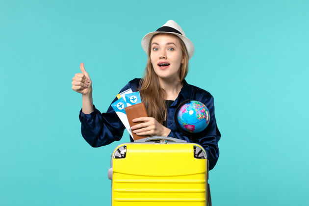 年轻女子正面图年轻女子拿着机票和地球仪在蓝色办公桌上乘机出海度假远航地球仪票举行