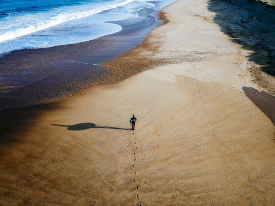海洋从在海岸线上行走的冲浪者身上射出的无人机冲浪板目的地沙滩