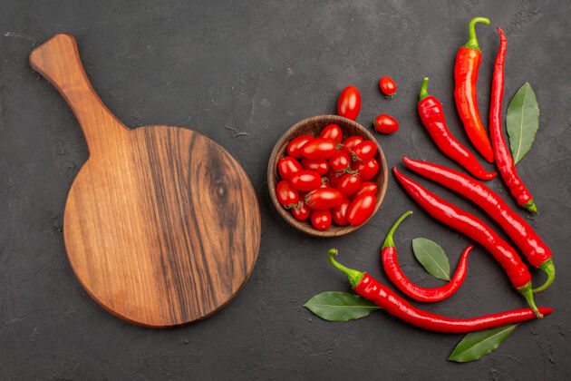 碗顶视图红辣椒和支付叶和一碗樱桃西红柿和一个椭圆形的砧板在黑色的桌子上与自由空间餐桌蔬菜胡椒