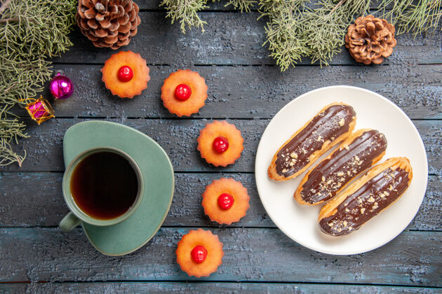 盘子俯视图：白色椭圆形平板上的巧克力蛋糕 冷杉树枝和圆锥体 圣诞玩具 纸杯蛋糕和一杯茶 放在深色木桌上蛋筒热的咖啡