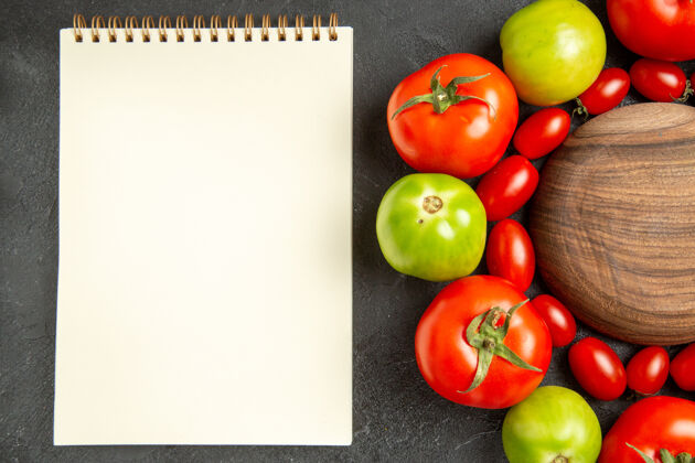 西红柿顶视图樱桃红色和绿色的西红柿围绕着一个木板和一个笔记本在黑暗的地面上蔬菜成熟顶部