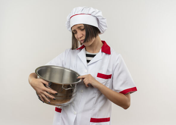 年轻体贴的年轻女厨师穿着厨师制服 手拿着锅 看着隔离在白墙上的锅人持有烹饪