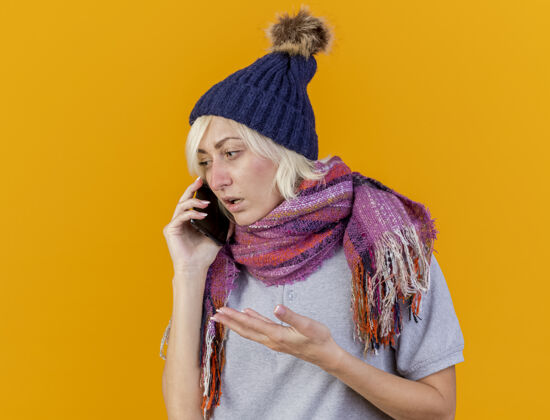 围巾笨手笨脚的年轻金发病斯拉夫女人戴着冬天的帽子和围巾在电话里说话看着身边疾病无知电话