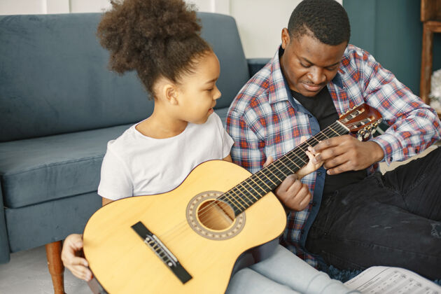 学习父亲带着女儿坐在沙发上女孩拿着吉他学吉他家庭玩耍房子