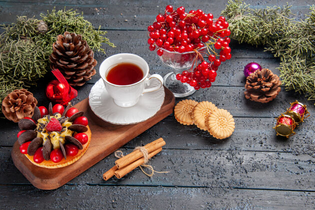桌子底部视图一杯茶和浆果蛋糕放在木制盘子里葡萄干放在玻璃松果里圣诞玩具冷杉树叶放在深色木制桌子上杯子蛋糕底部