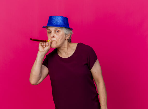 聚会自信的老太太戴着派对帽吹着口哨看着粉色的相机老人帽子女人