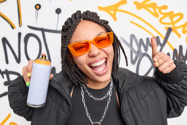 太阳镜时髦的美国黑人少女微笑着在城市里摆出溜溜球的姿势用喷雾画涂鸦戴墨镜和夹克属于流氓团伙艺术家文化时髦