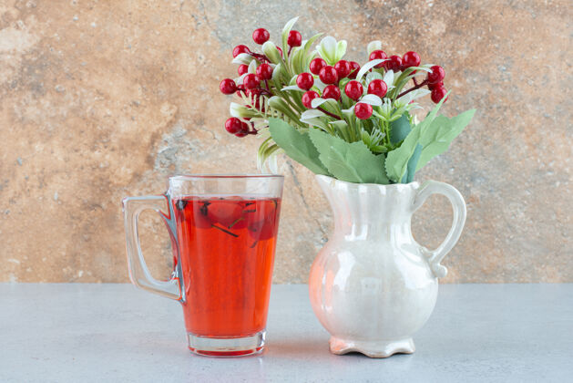 柠檬水蓝色桌子上有一杯玫瑰果和人造花的果汁美味玻璃果汁