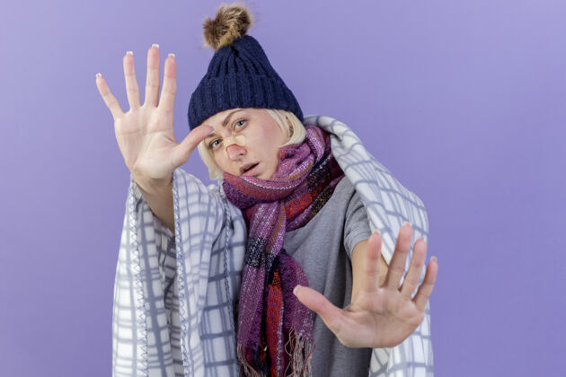 疾病自信的年轻金发病斯拉夫女人鼻子上贴着医用膏药戴着冬天的帽子和围巾鼻子医学包装