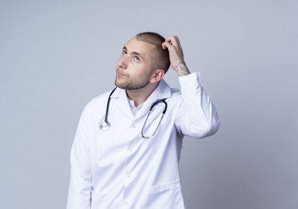 听诊器体贴的年轻男医生 穿着医用长袍 脖子上戴着听诊器 抬头望着 隔着白墙搔着头人抓挠周围
