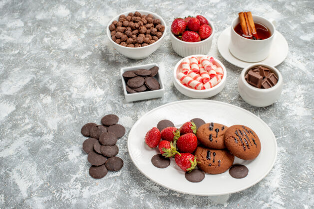 谷类食品底视图饼干草莓和圆形巧克力放在椭圆形的盘子里 糖果草莓巧克力麦片和肉桂茶放在灰白色的桌子上水果碗草莓