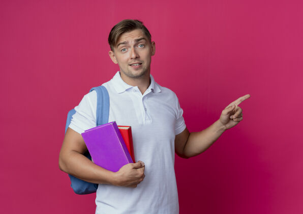 点印象深刻的年轻英俊的男学生穿着背包拿着书和分在一边学生印象粉红色