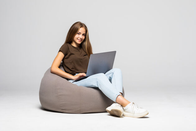 微笑快乐的年轻女子坐在地板上用笔记本电脑在灰色的墙上学习大学坐着