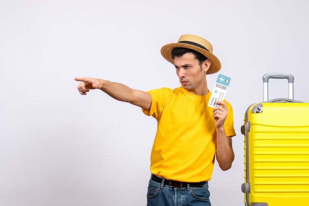 男正面图穿着黄色t恤的年轻游客站在黄色手提箱旁指着什么东西站立前面男