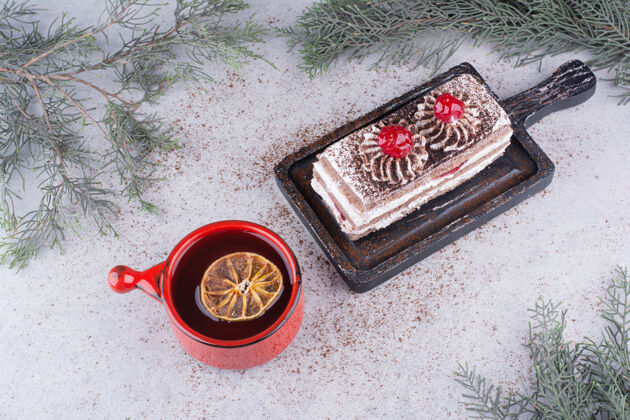 蛋糕在深色的木板上放一块奶油蛋糕和一杯茶杯子甜点橙子