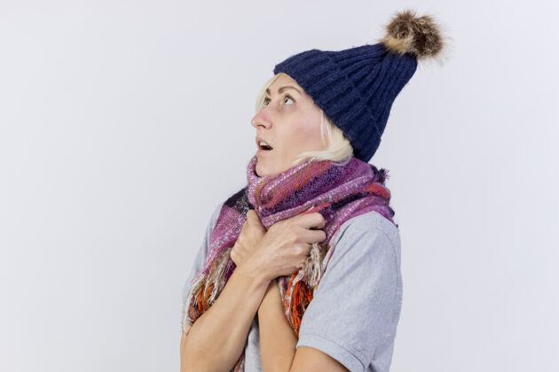 穿着焦虑的年轻金发病女人戴着冬天的帽子 拿着围巾 孤零零地看着白色的墙上金发人斯拉夫