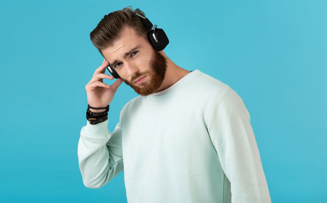 耳机留胡子的男人在蓝色的无线耳机上听音乐的肖像耳机人物立体声