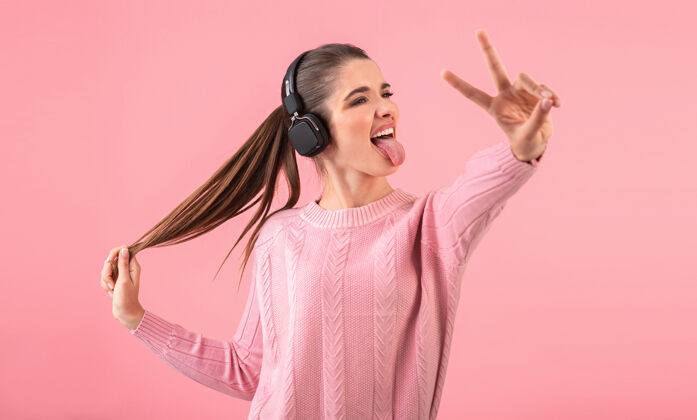 无线戴着无线耳机听音乐的年轻女子穿着粉色毛衣微笑着摆出粉色的姿势科技欢乐耳机