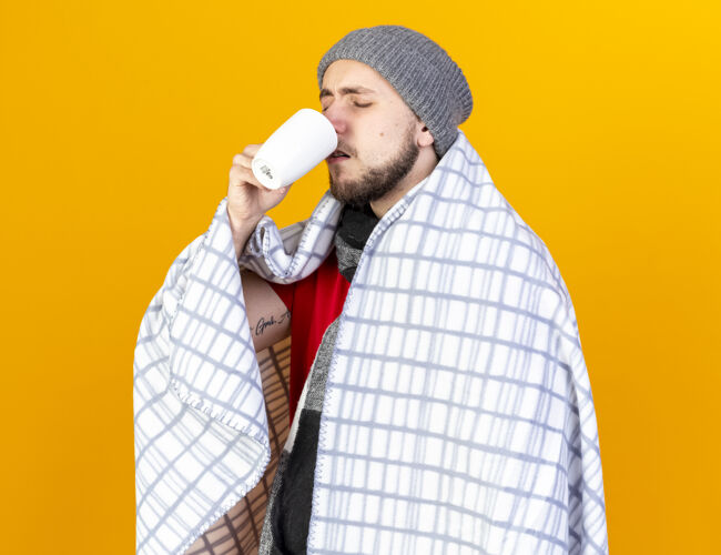 人一个戴着冬日帽子 围着方格围巾 喝着一杯隔离在橘色墙上的茶的年轻人人人冬天