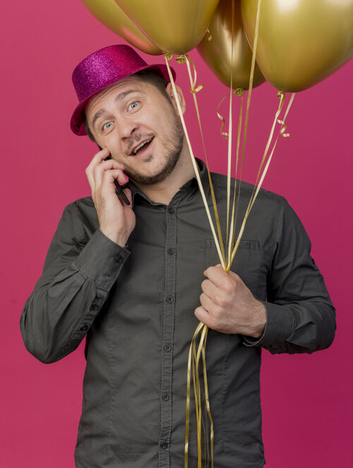 电话面带微笑的歪着头的年轻人戴着粉红色的帽子拿着气球在电话里说孤立的粉红色粉色年轻人说话