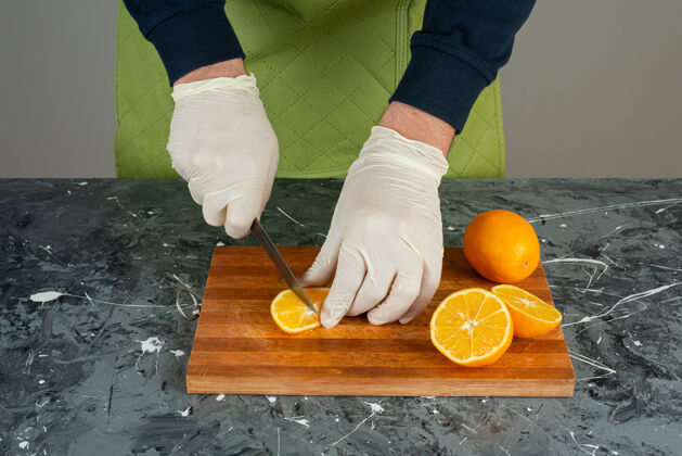 有机男性手戴手套在大理石桌上切橘子汁各种男围裙