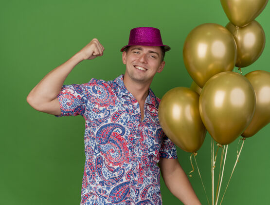 年轻面带微笑的年轻人戴着粉红色的帽子拿着气球 表现出强烈的姿态孤立在绿色展示帽子粉色