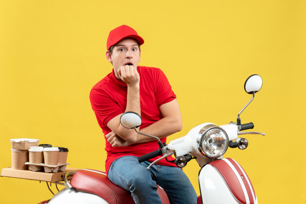 人前视图是一个体贴的年轻人 穿着红色上衣 戴着帽子 在黄色背景下下达命令摩托车男人微笑