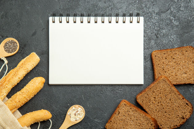 面包深灰色表面上的面包和黑面包的俯视图记事本黑板勺子