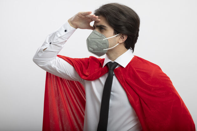 领带年轻的超级英雄戴着领带和医用面罩看着远处 手被隔离在白色医疗距离超级英雄