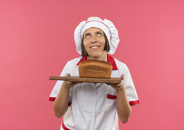 衣服身着厨师制服的年轻女厨师面带微笑 手里拿着放着面包的砧板 孤零零地看着粉红色的墙上女性厨师感情