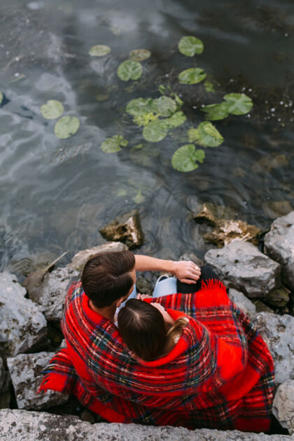 拥抱美丽的年轻夫妇坐在石堤上 裹着毯子年轻放松抱着