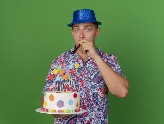 穿高兴的年轻人戴着蓝帽子 拿着蛋糕 吹着绿色的聚会吹风机抱着派对帽子
