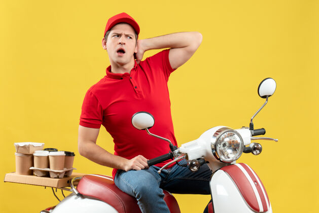 摩托车戴着红色上衣和帽子的困惑的年轻人在黄色背景下传递命令的俯视图命令帽子微笑