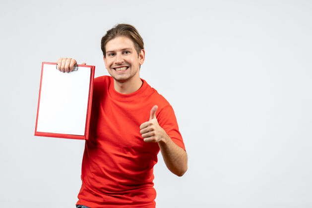 成人正面图是一个微笑的年轻人 穿着红色上衣 手里拿着文件 在白色背景上做着“ok”的手势制造微笑男性
