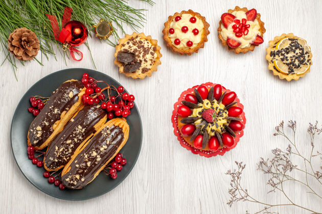 晚餐顶视图巧克力eclairs和醋栗在灰色的盘子馅饼浆果蛋糕和松树叶子与圣诞玩具在白色的木桌上圣诞沙拉酸