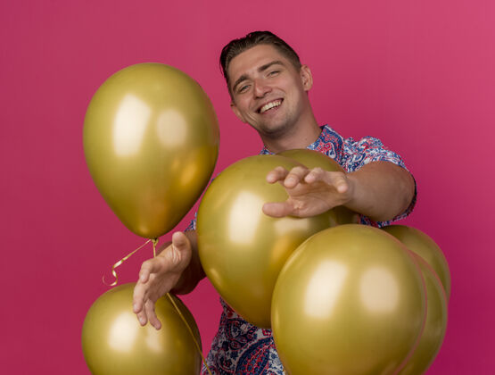 抱着身着五颜六色衬衫 面带微笑的年轻人站在气球后面 手孤立地伸出粉红色的手派对气球粉色