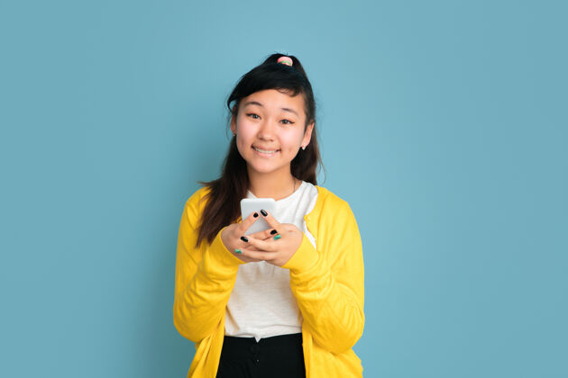 女性在蓝色工作室背景上孤立的亚洲青少年肖像美丽的深褐色长发女性模特人类情感的概念 面部表情 销售 广告使用电话 微笑人衬衫手