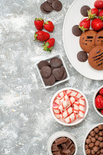 食物顶视图饼干草莓和圆形巧克力在椭圆形盘子碗糖果草莓巧克力谷类食品在灰白色的桌子右侧碗浆果水果