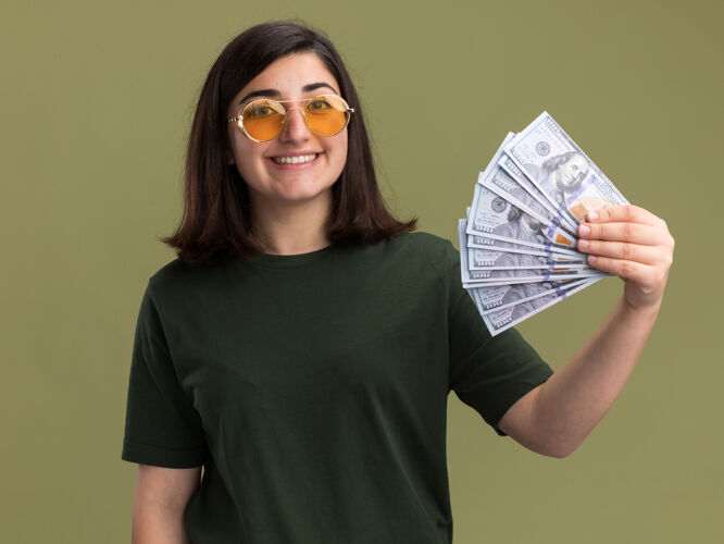 漂亮戴着太阳眼镜的年轻漂亮的白人女孩微笑着拿着橄榄绿的钞票微笑金钱年轻