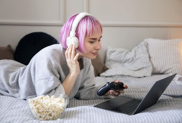 技术粉红色头发的年轻女子在玩笔记本电脑上的操纵杆视频游戏乐趣室内