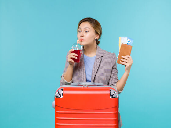 杯子正面图：度假中的女性手持一杯新鲜果汁和蓝色背景上的机票旅行飞机度假旅行海上冷冻甜点成人旅行
