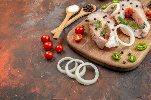 左新鲜生鱼和胡椒洋葱绿色西红柿的侧视图在混合色表面左侧的木制砧板上菜肴美味切