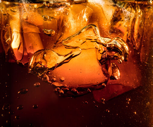 液体深色可乐背景下冰块的特写镜头玻璃壁上有泡沫和大气泡的清凉甜味夏季饮料的质地起泡或漂浮到表面顶部冷凝起泡可乐
