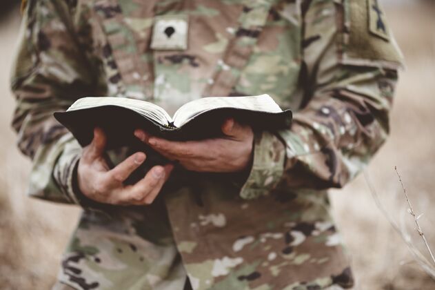 军队一个年轻士兵拿着一本打开的圣经在田野里的浅焦镜头精神宗教男性