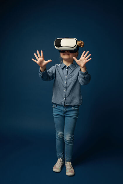 创新仙女的第一步穿着牛仔裤和衬衫的小女孩或孩子 在蓝色工作室背景上隔离虚拟现实耳机眼镜尖端技术的概念 视频游戏 创新网络软件游戏