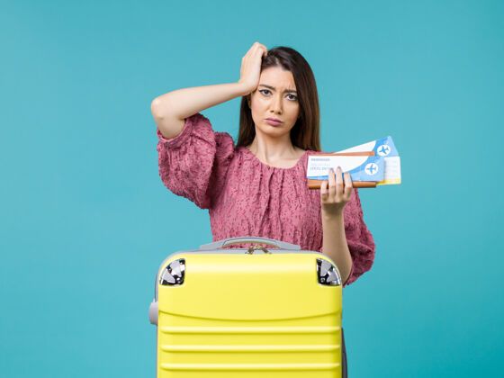 人正面图：度假中的女性拿着蓝色背景的机票旅行夏季旅行女性海上度假票担心肖像